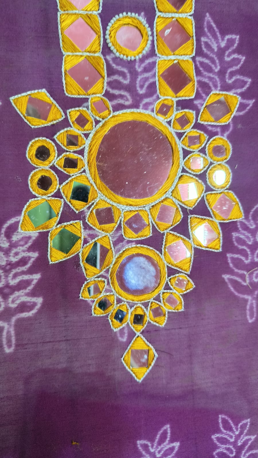 Close-up of hand-stitched mirror work in gold thread on couture fabric